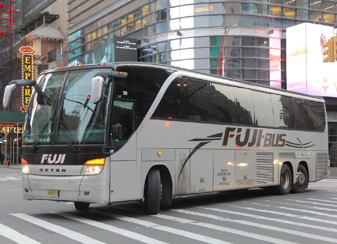 A Fuji Bus coach in a cityscape stops at an intersection. This image captures the bus's exterior with surrounding urban elements like billboards, buildings, traffic lights, and street markings.