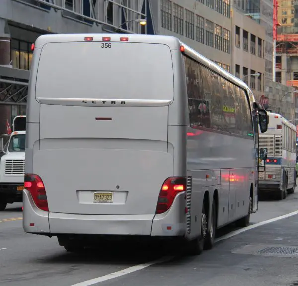 Rear view of a silver coach bus with license plate D17327 on a city street, surrounded by buildings and other vehicles.