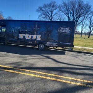 A Fuji moving truck is parked on the side of a road in a park area with bare trees and a clear blue sky.